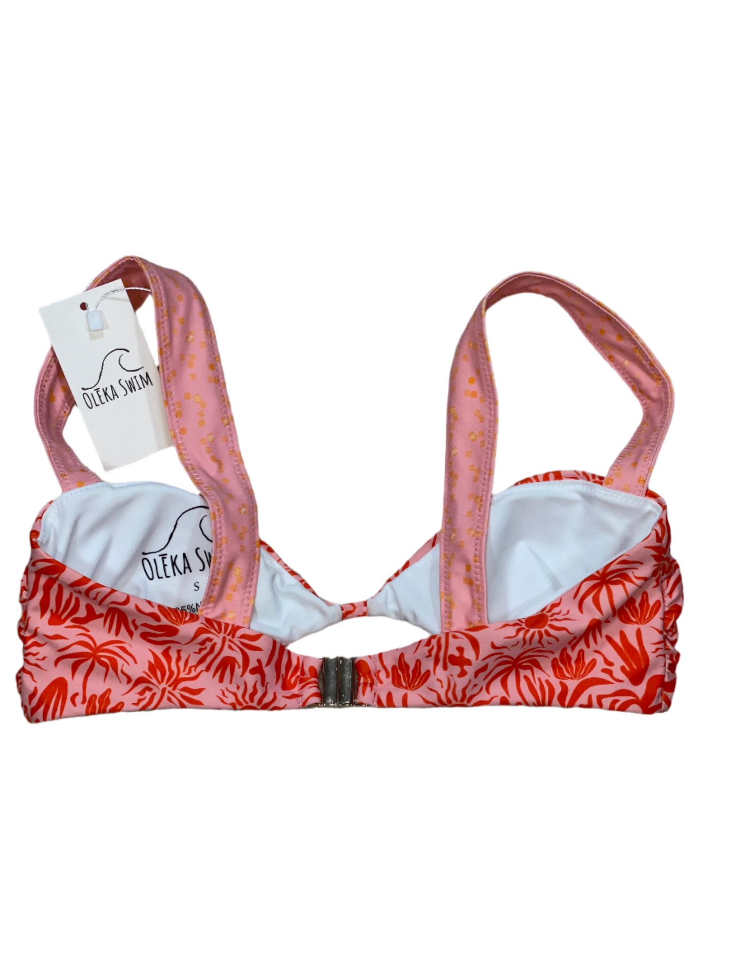 The Lola bikini top in a red and pink tropical pattern, featuring sun motifs and palm leaves. The top has wide pink straps with a subtle dot pattern and a clasp closure at the back. The bikini top is displayed flat on a white background with a tag attached, labeled 'Oleka Swim.