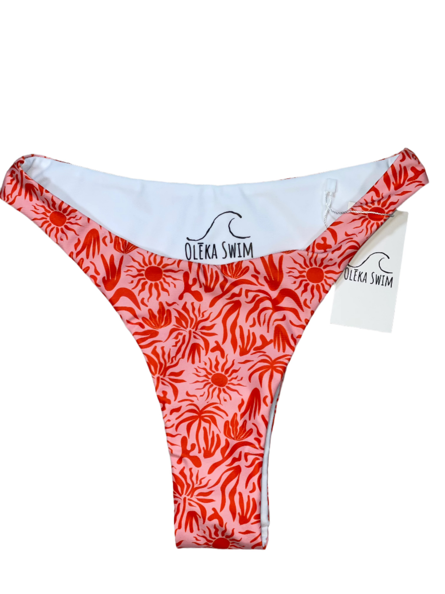 The Lola bikini bottom in a vibrant red and pink tropical pattern, featuring sun motifs and palm leaves. The bikini bottom is displayed flat on a white background with a tag attached, labeled 'Oleka Swim.