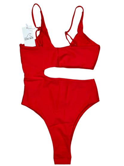 The Nala One Piece swimsuit from Oleka Swim, displayed flat on a white background. The swimsuit is a vibrant red color, featuring a stylish cutout on the side and adjustable shoulder straps. A tag reading 'Oleka Swim' is attached to the swimsuit.